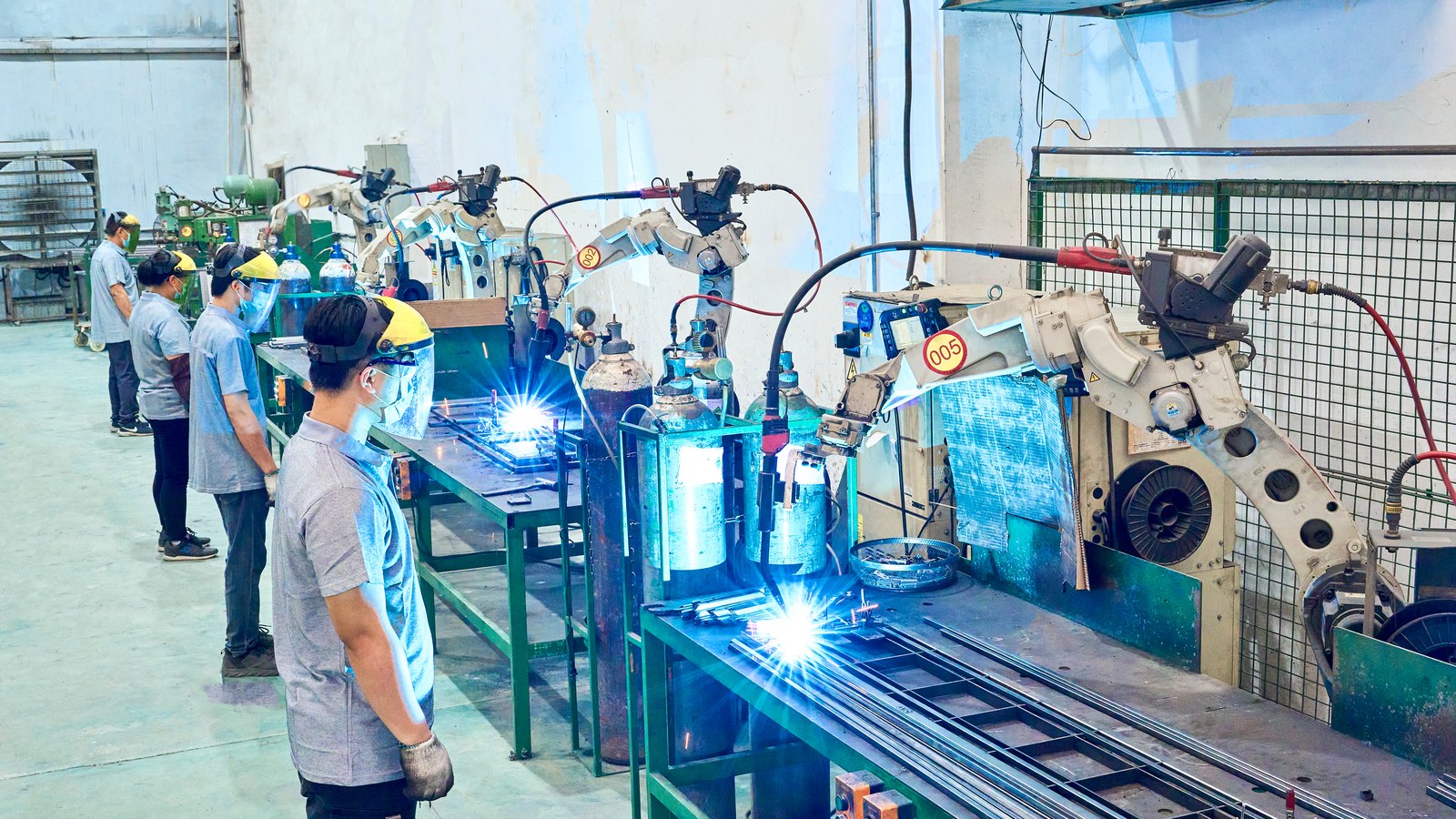 Robotic welding cells producing metal fixture frames under operator supervision